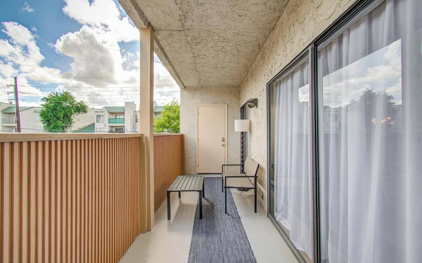 Un balcon avec une table et des chaises, une porte-fenêtre coulissante et une vue sur le ciel et les bâtiments.