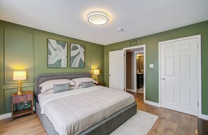 Une chambre à coucher avec un lit, deux lampes de chevet, une porte et un couloir menant à une salle de bain.