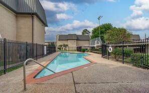 A swimming pool with a metal fence, a brick building, and a clear sky.