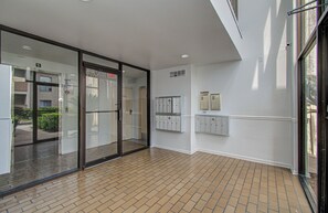 A hallway with a glass door, a tiled floor, and a wall-mounted storage unit.