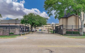 A gated parking area with a clear sky, trees, and a building with a brick facade.
