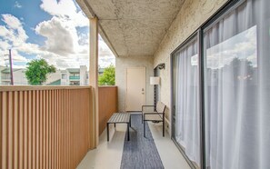 A balcony with a table and chairs, a sliding glass door, and a view of buildings and trees.