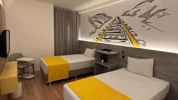 A hotel room with two single beds, a desk, a chair, and a wall-mounted TV.