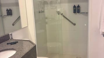 A bathroom with a granite countertop, a white toilet, a glass-enclosed shower, and a mirror.