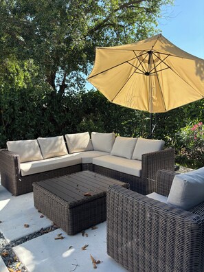 Ein modulares Sofa mit Kissen, ein Korbtisch und ein großer Sonnenschirm, der Schatten spendet.