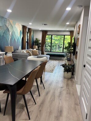 Una sala de estar moderna con comedor, ventanas amplias y vistas a zonas verdes.
