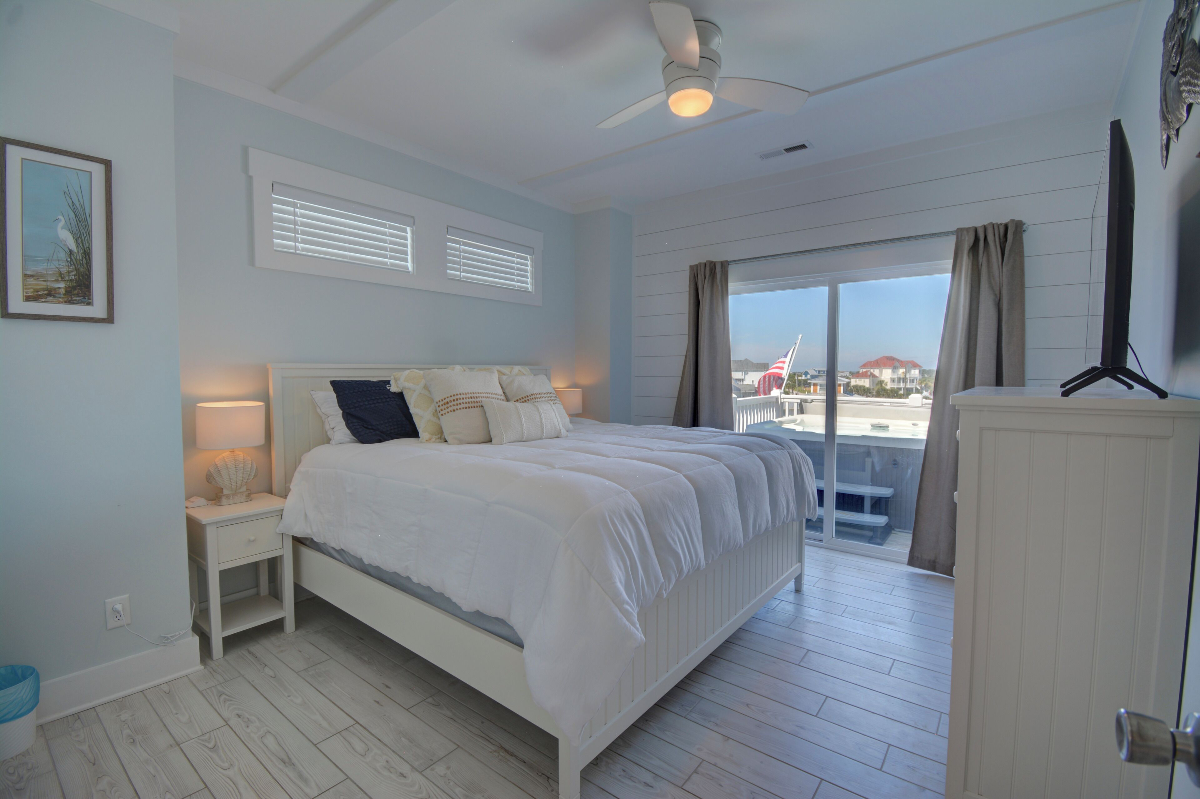 A bedroom with a bed, bedside tables, a ceiling fan, and a view of the outside.