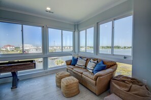 A spacious room with a large window, a leather sofa, and a piano. - Soundfront 3BR home with pool, hot tub, dock, and ocean access. (North Topsail Beach)
