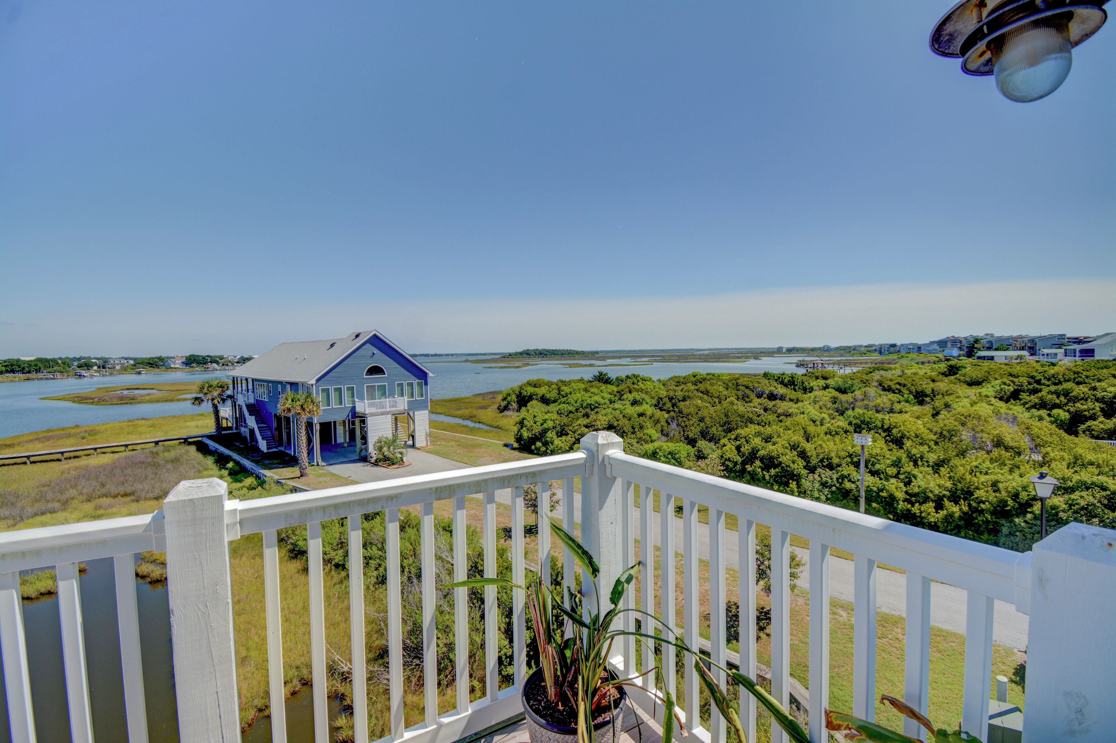 A coastal house with a balcony, a view of the water, and surrounding greenery.