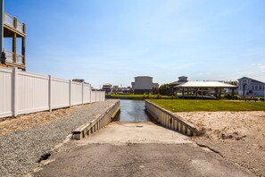 A waterfront property with a concrete walkway leading to a small water channel, surrounded by a white fence and a grassy area. - Soundfront 3BR home with pool, hot tub, dock, and ocean access. (North Topsail Beach)
