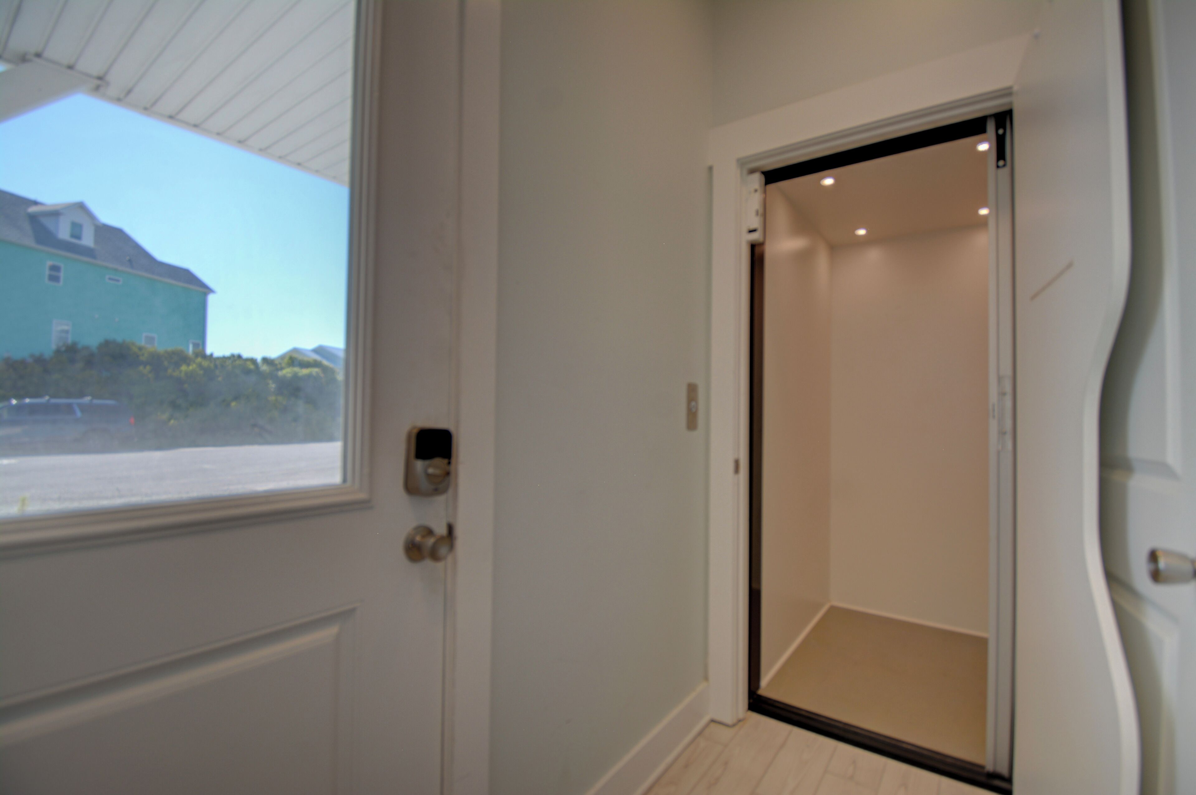 Una habitación con una puerta que da a un ascensor, una ventana con vista a un edificio, y una puerta con manija.