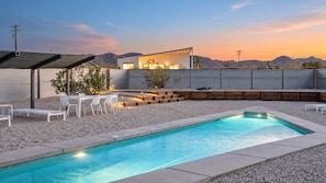 Una piscina con area prendisole, immersa in un paesaggio ghiaioso e affiancata da una casa moderna con tetto a falda.