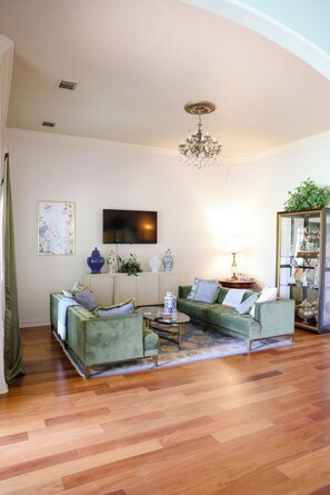 Un salon avec un canapé vert, un téléviseur à écran plat, un lustre et un meuble décoratif.