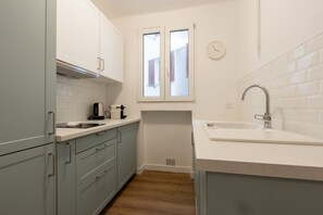 Eine Küche mit hellblauen Schränken, einer weißen Arbeitsplatte, einem Fenster und einem Spülbecken.