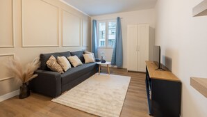 Ein modernes Wohnzimmer mit einem dunkelgrauen Sofa, einem kleinen runden Tisch und einem Fernseher auf einem Holzboden.