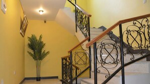 A staircase with ornate black railings, a potted plant, and a yellow wall.