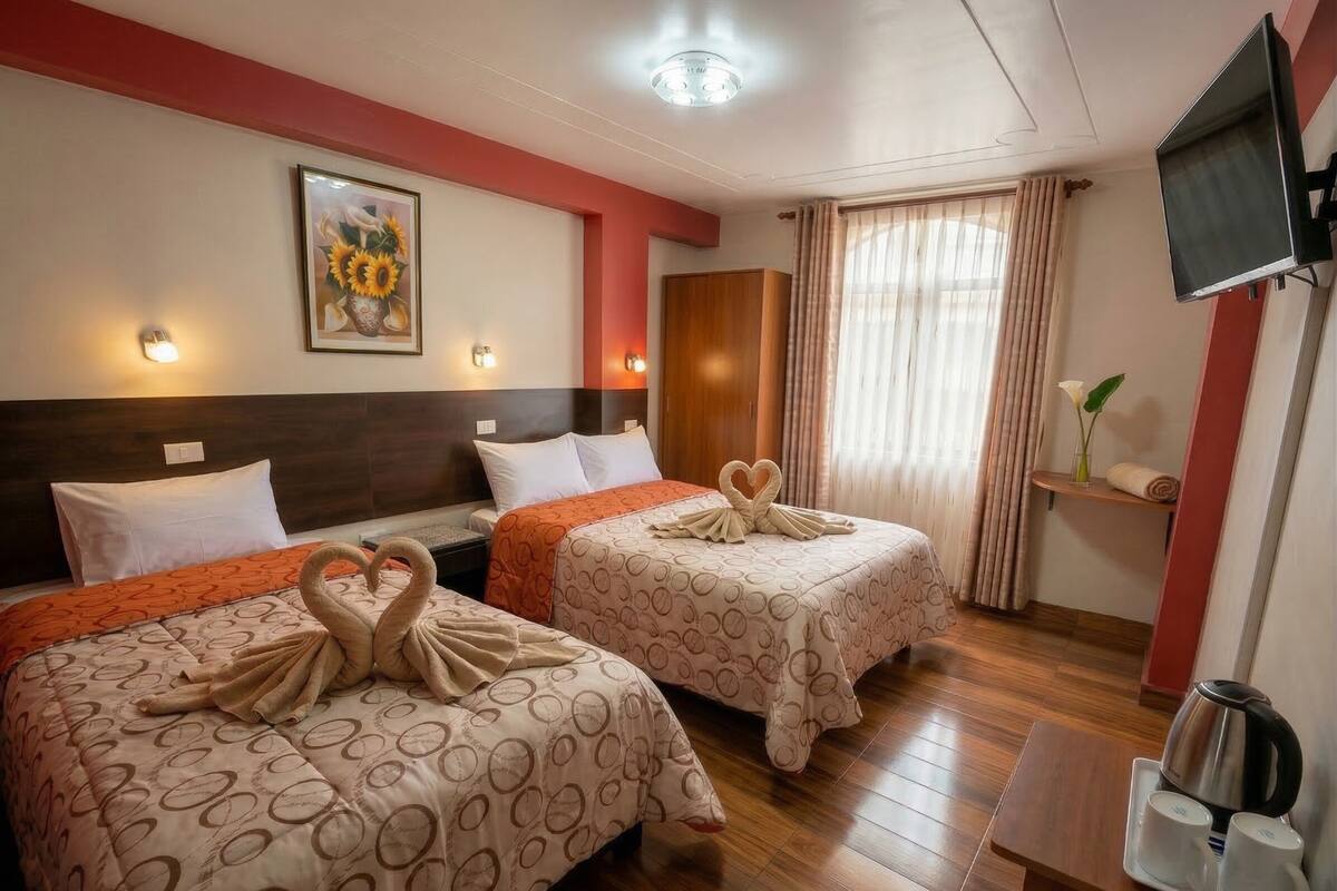 Habitación de hotel con dos camas, televisión, un cuadro y una zona para café.