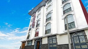 A multi-story hotel with a prominent red sign, large windows with decorative iron grilles, and a stone facade.