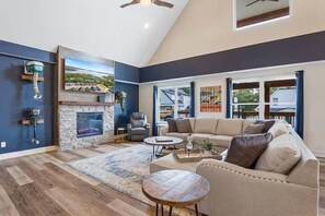 A living room with a fireplace, a sofa, a coffee table, and a view of the outdoors. - Shore Thing | Steps to Pool | Hot Tub + Pool Table (Hollister)