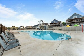 A swimming pool with lounge chairs, a water slide, and a building with balconies. - Shore Thing | Steps to Pool | Hot Tub + Pool Table (Hollister)