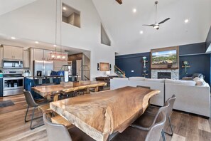 A spacious living area with a large wooden dining table, a sofa, and a TV mounted on the wall. - Shore Thing | Steps to Pool | Hot Tub + Pool Table (Hollister)