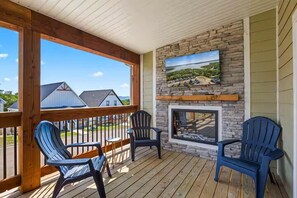 A covered deck with Adirondack chairs, a stone fireplace, and a view of houses. - Shore Thing | Steps to Pool | Hot Tub + Pool Table (Hollister)