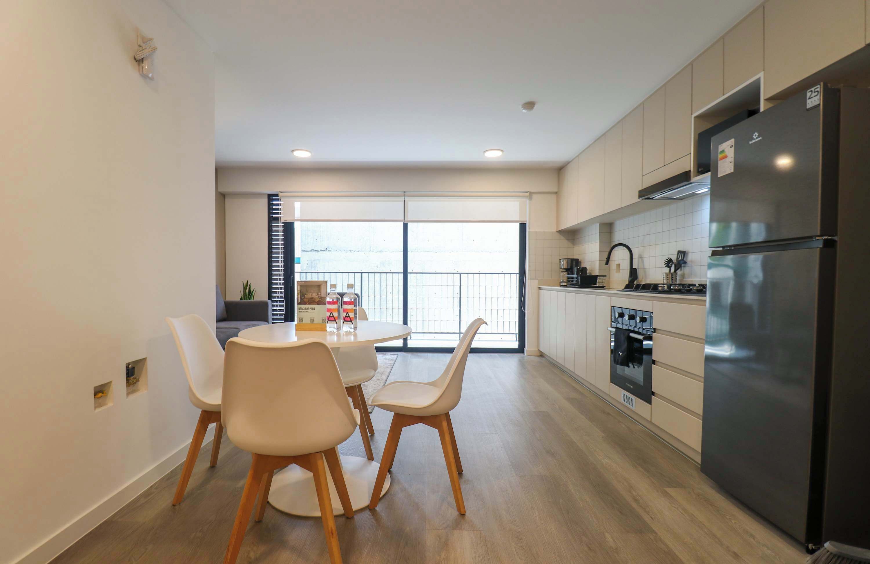 A modern kitchen with a refrigerator, oven, and dining area with chairs and a table.