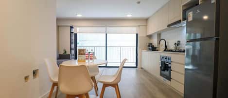 A modern kitchen with a refrigerator, oven, and dining area with chairs and a table.
