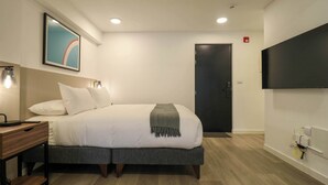 Una habitación de hotel moderna con cama, mesita de noche, lámpara, una obra de arte y televisión.