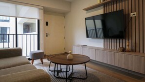 Ein modernes Wohnzimmer mit einer Couch, einem runden Tisch, einem an einer Holzwand montierten Fernseher und einer Schiebetür, die auf einen Balkon führt.