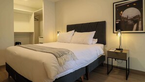 Ein ordentlich bezogenes Bett mit Kopfteil, einer Nachttischlampe und einem gerahmten Bild an der Wand.