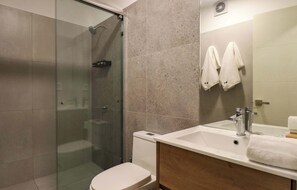 A modern bathroom with a glass shower enclosure, a white toilet, a sink with a mirror, and two towels hanging on the wall. - w* | Trendy & Cozy 2BR w/ Balcony in Miraflores (Miraflores)