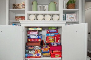 Eine Küche mit einem weißen Kühlschrank, Regalen voller Küchenutensilien und einer Auswahl an Gesellschaftsspielen.