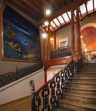 A grand staircase with ornate black railings, a large mural depicting a night scene with boats, and a wooden ceiling with exposed beams.