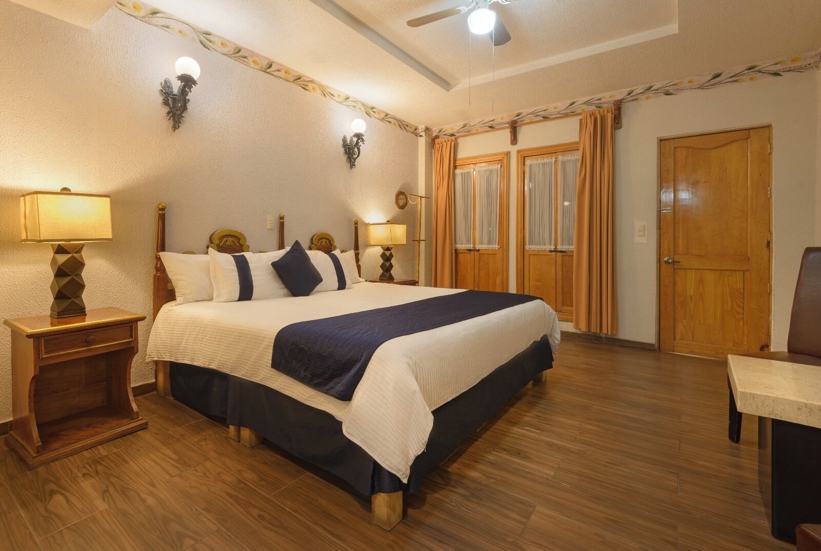 A hotel room with a large bed, two bedside tables with lamps, a wooden door, and a ceiling fan.