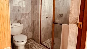 A bathroom with a toilet, a shower with a glass door, and tiled flooring. - HOTEL BOUTIQUE GRAND MAYES (Pátzcuaro)