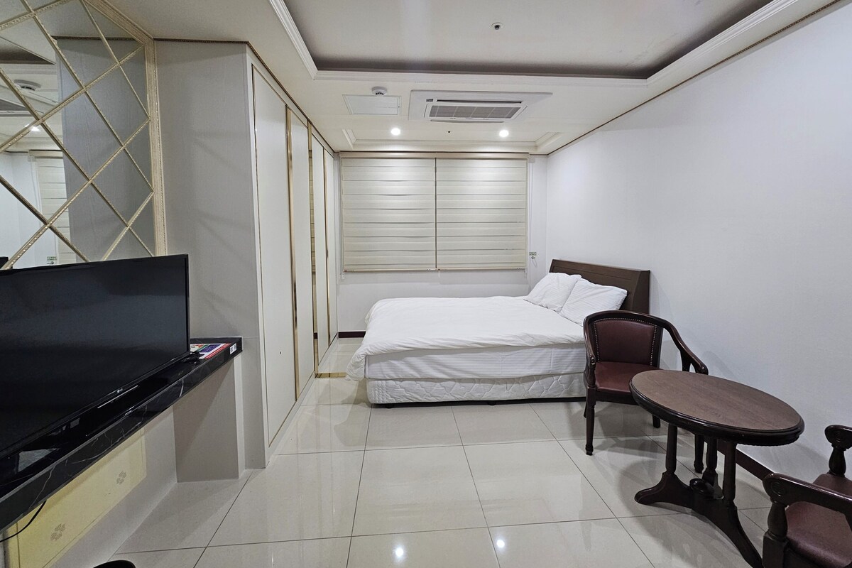 A hotel room with a bed, a TV, a small table, and a chair.