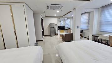 A hotel room with two beds, a kitchenette, a TV, and a window with blinds.