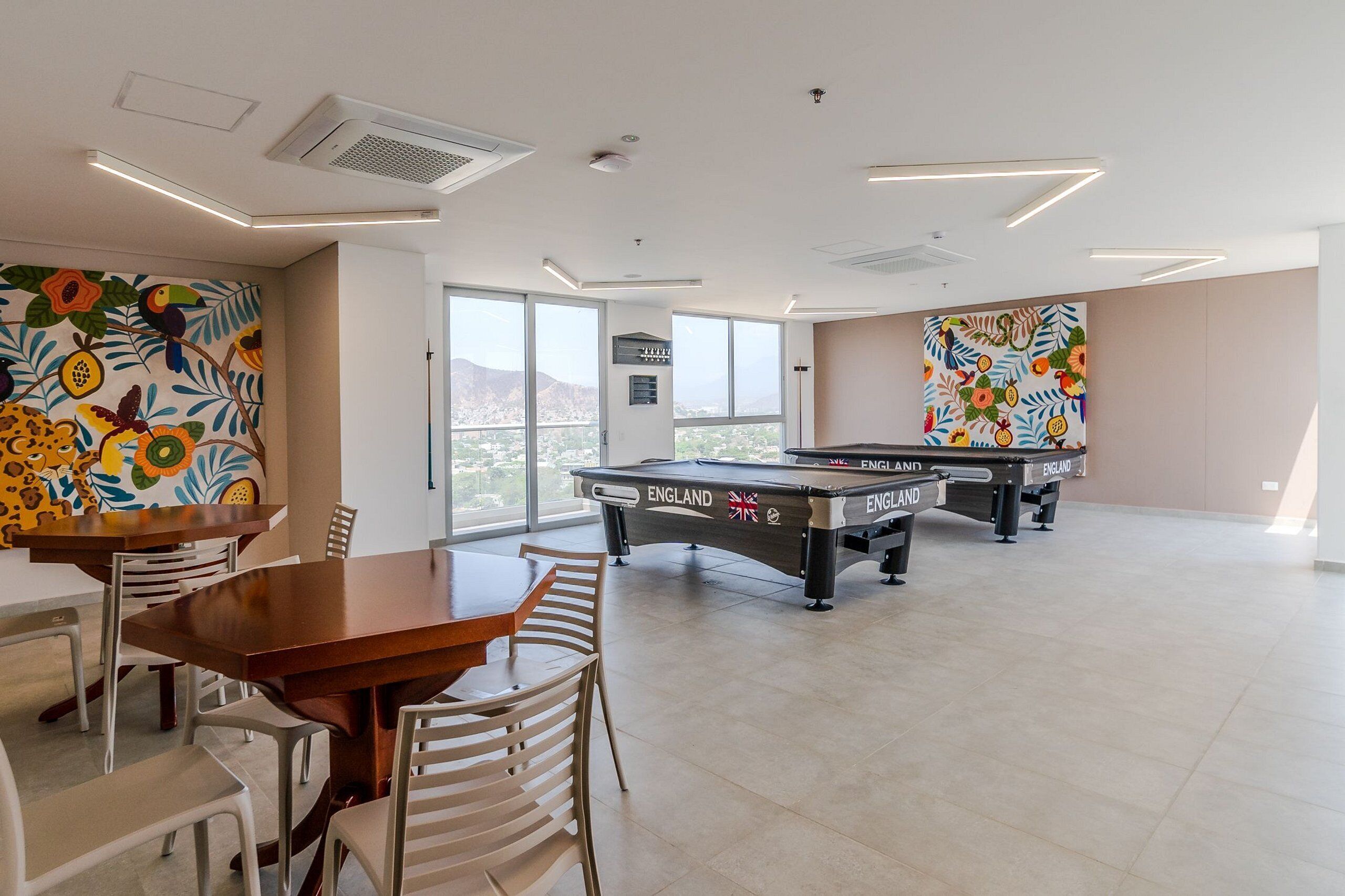 A spacious room with a pool table, dining area, and large windows offering a city view.