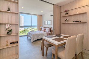 A modern hotel room with a large bed, a dining table, and a view of the city. - Salguero Suites by RV Stays (Santa Marta)