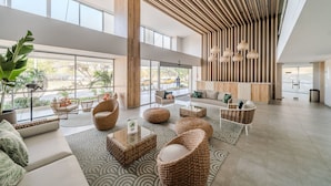Un lobby espacioso con techos altos, ventanas grandes y una variedad de espacios de descanso, incluyendo sofás y sillones de mimbre.