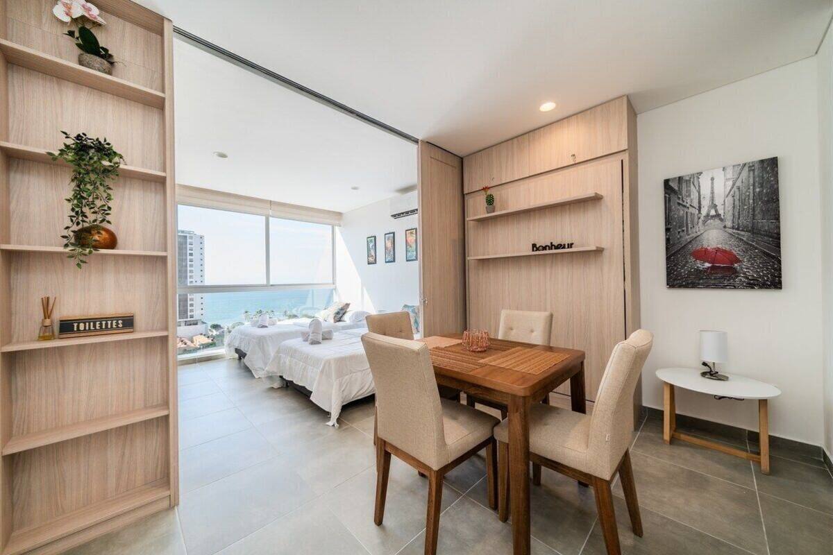 Ett modernt hotellrum med ett matbord i trä, beige stolar, ett litet sidobord och utsikt över staden.