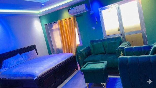 A room with a bed, a green sofa, a small table, and a window with curtains. - Serene Mountain Escape: Cozy Villa with Stunning Sunset Views (Freetown)
