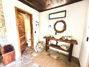 A bathroom with a wooden door, a white sink with a mirror, a towel rack, and a small shelf with toiletries.