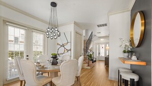 Una zona pranzo con tavolo in legno, sedie imbottite bianche, un lampadario e una scala che conduce a un'altra stanza.