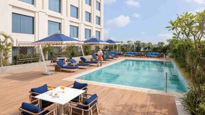 A hotel pool area with lounge chairs, umbrellas, and a dining table.