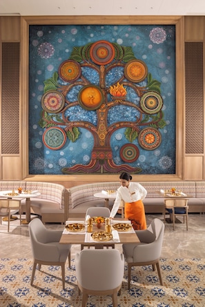 A dining area with a large mural, a woman serving, and a patterned floor.