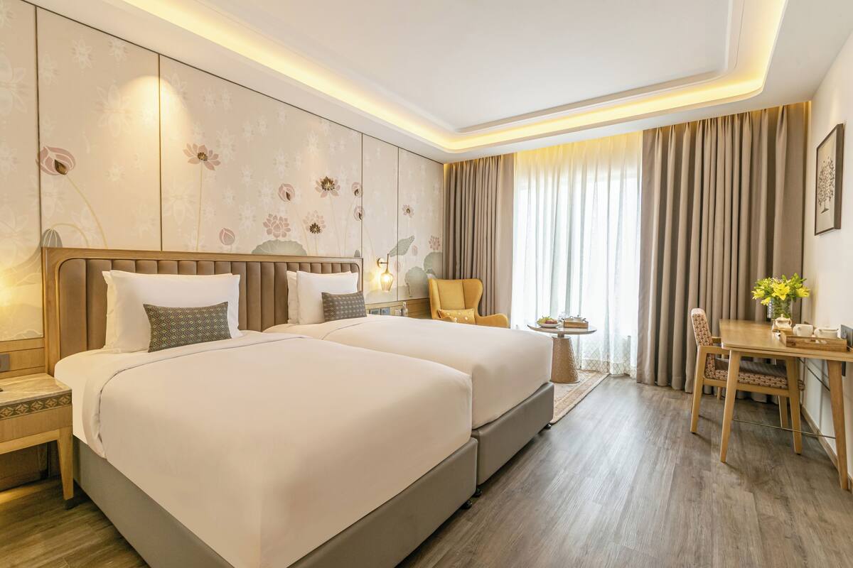 Habitación de hotel con una cama grande, un escritorio, una silla y un ventanal con cortinas.