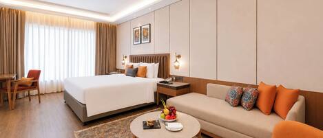 A hotel room with a bed, a sofa, a small table, a chair, and a nightstand.