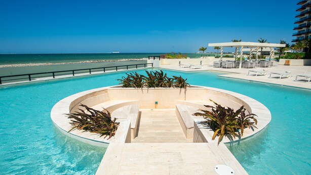 Ein Pool mit freiem Blick auf den Ozean, umgeben von Liegestühlen und einer Pergola.